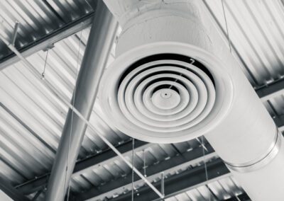 Black and white photo of an industrial air duct system showing spiral vents and structural beams.